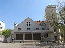 Église du XXe siècle. Clocher une tour octogonale sur le côté surmontée d'une croix domine un parvis.