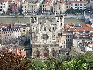 Photographie aérienne couleur de la façade d'une cathédrale, sur fond de cours d’eau.