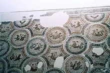 Vue partielle d'une mosaïque posée sur un mur, avec des médaillons et une bordure endommagée
