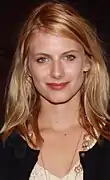 Portait d'une jeune femme aux yeux clairs et aux cheveux blonds-roux tombant devant ses épaules. Souriant légèrement, elle regarde le photographe.