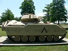véhicule blindé de couleur sable vu de profil dans un parc arboré