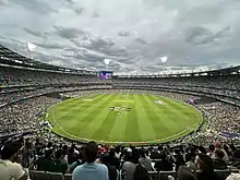 Vue panoramique de l'intérieur d'une enceinte sportive avec des tribunes remplies avant une rencontre de cricket.