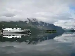Un bateau sur un lac entouré de montagnes, sous un ciel nuageux.