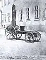 Photo d'une voiture, en apparence une planche avec quatre roues avec une potence et un siège rudimentaire.