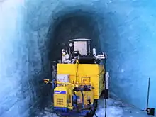 Un engin de forage jaune dans un tunnel de glace bleutée.