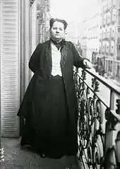 Photo en noir et blanc d'une personne debout de face sur son balcon.