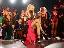 Madonna dans une salle de spectacle, assise en robe de scène devant ses danseurs