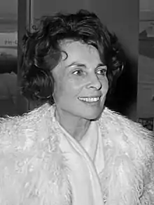 Photographie en noir et blanc d'une femme brune souriante d'âge moyen, en manteau élégant.