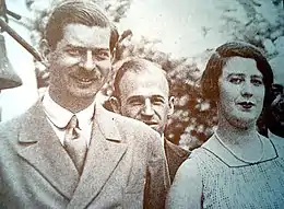 Photo noir et blanc en buste d'un couple suivi d'un homme dont on ne voit que la tête.