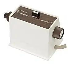 Une boîte blanche avec un dessus marron avec deux molettes et un bouton noir.
