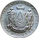 Pièce de monnaie comprenant un bouclier avec un pin, sous l'arbre un élan couché, deux figures masculines, l'une portant une faux , l'autre une ancre et les inscriptions Dirigo, Maine, UNITED STATES OF AMERICA et HALF DOLLAR.