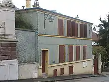 Photographie couleurs d'une maison à deux niveaux à volets rouges.
