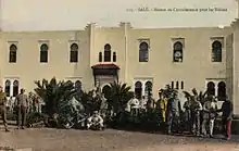 Photographie en couleur d'un bâtiment et des gens alignés devant pour poser pour la photo