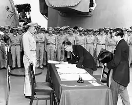 Shigemitsu signe les actes de capitulation devant Sutherland. Second plan : rangs de soldats américains.