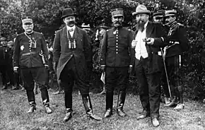 Photographie noir et blanc de 4 hommes debout, deux en uniforme et deux en civil.