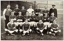 Photographie en noir et blanc d'une équipe de football. Quatre joueurs sont par terre, sept sont assis et sept autres sont debout, tous de face.