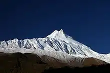 Montagne avec une double cime, enneigée et présentant des corniches de glace sous un ciel bleu profond.