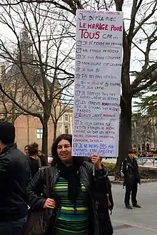 Une femme lors d'une manifestation à Toulouse. Elle tient une pancarte « cocher la case correcte, Je défile pour le mariage pour tous car... » où toutes les propositions sont cochées. Celles-ci sont « Je défend ma famille », « Ma famille me défend », « Je suis bonne citoyenne », « Mon couple est lesbien », « Je suis bi », « J'ai des amis hétéros qui ne veulent pas d'enfant » (le pas est souligné), « Je suis catho », « Je défends tous mes élèves - mêmes les hétéros », « les parents homoparentaux que je connais sont de bons parents » (« homo » et « bons » sont écrits d'une autre couleur), « égalité, liberté, fraternité », « je veux offrir aux petits français la même chance qu'ont les petits belges, espagnols, argentins, canadiens, danois », « je ne ments pas aux enfants, être gay est naturel ! » (« pas » est souligné).