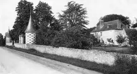 Photographie en noir et blanc d'une ancienne demeure et son mur d'enceinte.