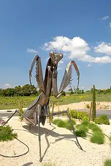 Sculpture de mante religieuse au rond-point à l'entrée du village