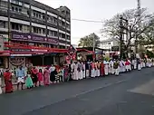 Photographie couleur d'une chaîne humaine comptant des adultes et des enfants en costumes indiens dans une rue.