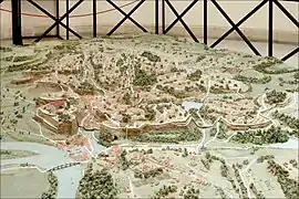 Photographie en couleurs d'une maquette représentant un site de collines près d'un fleuve et quelques bâtiments.