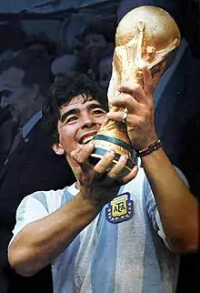 Un joueur de football souriant soulève un trophée des deux mains.