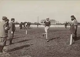 Un homme avec une casquette blanche passant près d'un poteau, d'autres hommes le regardent.