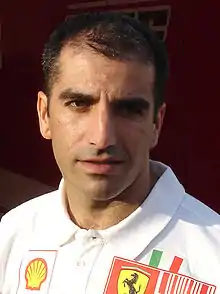 Photographie d'un homme, vu de face, en gros plan, brun, à la peau blanche légèrement bronzée, avec une tenue blanche pour Ferrari.