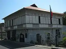 Une maison à étage. Une véranda ceint le premier étage, des panneaux coulissant permettant d'y accéder.