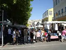 Petits stands d'un marché dans une large rue, à l'ombre des arbres