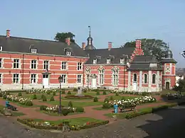 vue sur un jardin carré, derrière lequel s'élève un château rose à un étage, plus un étage sous un toit d'ardoise