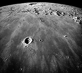 Image en plongée de la surface lunaire. Un petit cratère est visible au premier plan et un plus grand à l'arrière plan.