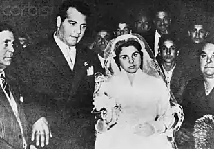 Image en noir et blanc avec à droite une femme en tenue de mariée, à gauche, un homme en costume, entourés par divers personnages.