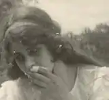 Photo en noir et blanc de la tête d'une femme, la main devant la bouche et un cerceau dans les cheveux