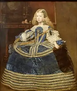 Jeune fille blonde, noble, en robe ample bleue, vue de face sur fond sombre. Scène d'intérieur