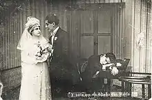 Photo en noir et blanc montrant à gauche un couple de jeunes mariés et à droite un homme endormi sur un bureau