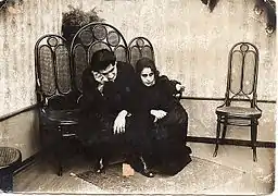 Photo en noir et blanc montrant un homme et une femme, habillés en noir, pleurant assis sur des chaises