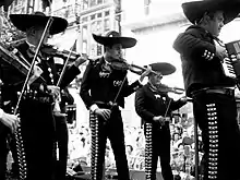 Photographie montrant un groupe de musiciens mexicains vêtus de tenues traditionnelles et coiffés de sombreros.