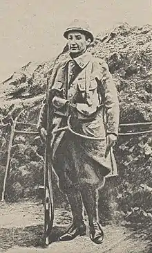 Une femme déguisée en poilu, arme à la main, dans les tranchées de la Première Guerre mondiale.