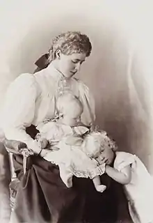 Vue noir et blanc d'une femme assise, un bébé assis sur ses genoux, une petite fille posant sa tête près du bébé.