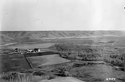 Photographie en noir et blanc de quelques bâtiments au centre d'une vaste vallée.