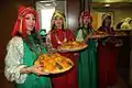 Marocaines en habits traditionnels présentant des plats de couscous.