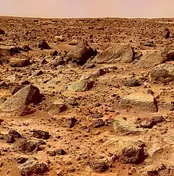 De grandes roches sont visibles sur un sol rougeâtre.