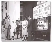 photo noir et blanc d'un groupe de quatre personnes à côté d'une pancarte marquée « American Unitarian Service Commitee - Distribution de lait - Août 1940, France »
