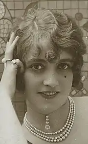 photographie en noir et blanc du visage d'une jeune femme aux cheveux courts vue de face, une mouche sur le joue gauche