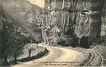 Carte postale ancienne montrant un virage serré de la route de Voiron à Saint-Laurent-du-Pont, avec la voie unique du VSP en accotement surplombé par une impressionnante falaise