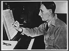 Photo : un homme au piano, écrit sur une partition posée sur le pupitre