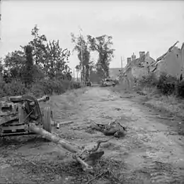 Photo montrant un canon antichar allemand détruit avec le corps d'un soldat allongé à côté et dans le fond un char Panther détruit