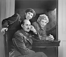 Photographie en noir et blanc de trois hommes posant de profil, installés autour d'une table.